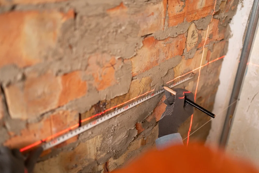 Repérage au crayon sur un mur de briques avec un mètre et un niveau laser