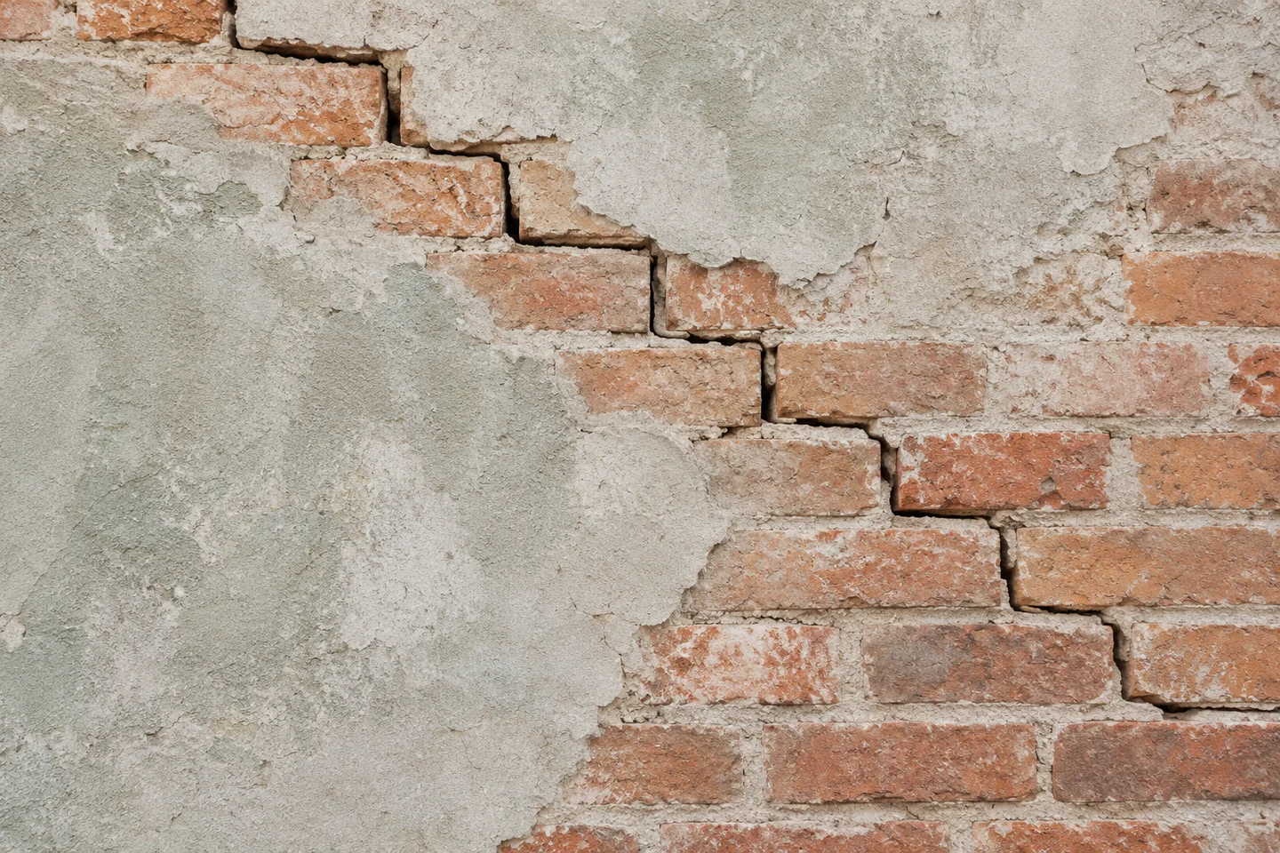 Fissure en marches d’escalier suivant les joints d’une maçonnerie de briques sous un enduit